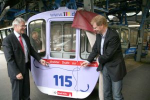 Eine Gondel der Kölner Seilbahn wirbt jetzt für die einheitliche Behördenrufnummer 115.