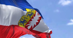 Wehende Flagge des Landes Schleswig-Holstein vor schwach bewölktem Himmel.
