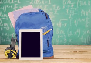 Schulranzen mit daran angelehntem Tablet, im Hintergrund eine grübe Kreidetafel.
