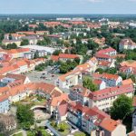 Luftaufnahme der Altstadt von Hoyerswerda, vorwiegend historische Häuser mit roten Ziegeldächern, im Hintergrund Bäume, im Vordergrund ein heller Kirchturm.