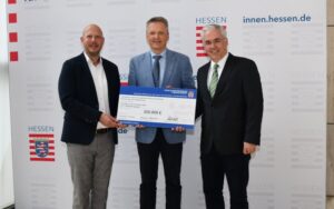 Von links halten Bastian Schäfer von der ekom21, Staatssekretär Martin Rößler und Prof. Dr.-Ing. Jörn Kohlhammer vom Fraunhofer IGD den Förderbescheid des Landes Hessen.