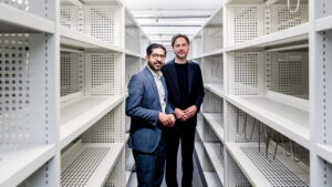 Hessens Wirtschaftsminister Kaweh Mansoori und Planungsdezernent Marcus Gwechenberger stehen zwischen leeren Regalmetern.