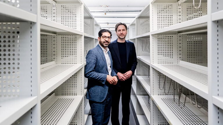 Hessens Wirtschaftsminister Kaweh Mansoori und Planungsdezernent Marcus Gwechenberger stehen zwischen leeren Regalmetern.