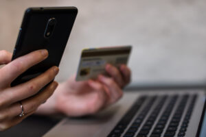 Hände, die eine Kreditkarte halten und Smartphone und Laptop verwenden.