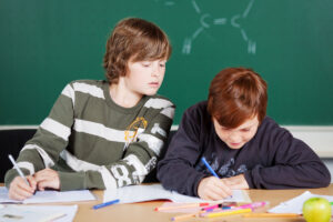 Ein Schulkind schaut seinem Nebensitzer über die Schulter, um abzuschreiben.