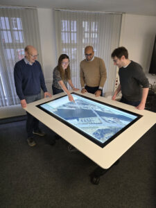 Das VIAA-Projektteam der Hansestadt Lübeck steht um einen Multitouchtisch versammelt.