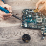 Computerteil-Reparatur: Ein paar Hne arbeitet mit einem Lötkolben an einer demontierten Hauptplatine.