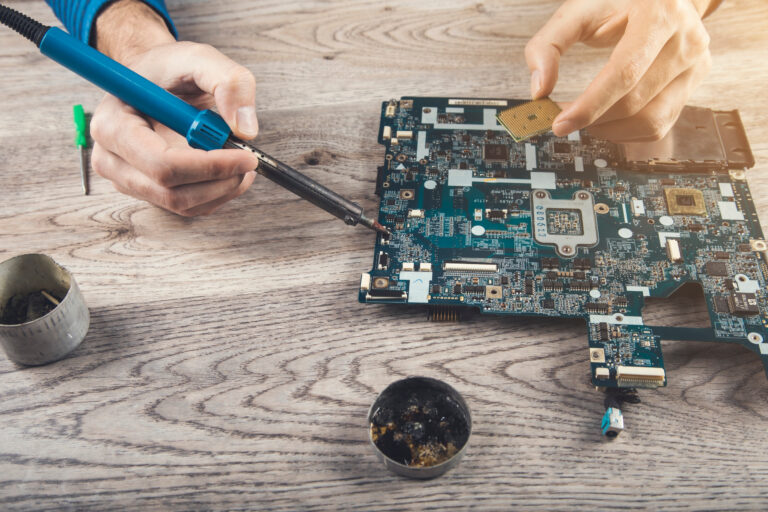 Computerteil-Reparatur: Ein paar Hne arbeitet mit einem Lötkolben an einer demontierten Hauptplatine.