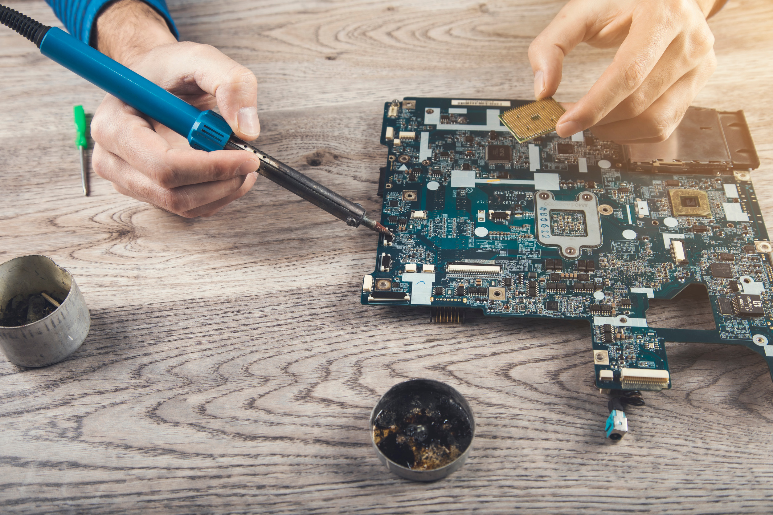 Computerteil-Reparatur: Ein paar Hne arbeitet mit einem Lötkolben an einer demontierten Hauptplatine.