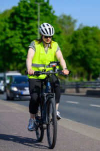 Eine Frau fährt mit einem Fahrrad eine Straße entlang, am Lenker ist eine Kamera befestigt.