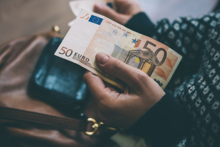 Frauenhände halten einen 50 Euroschein in der linken Hand, in der rechten ist undeutlich eine EC-Karte zu erkennen.