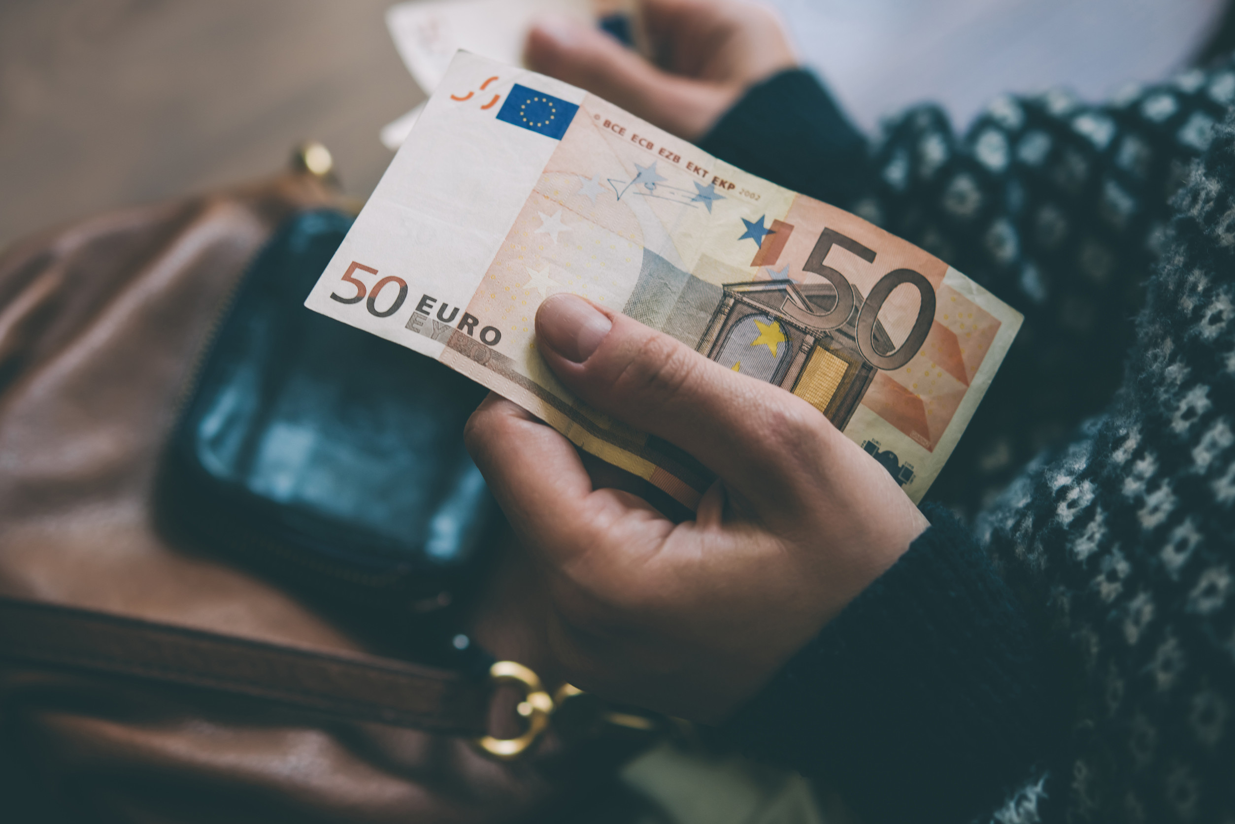 Frauenhände halten einen 50 Euroschein in der linken Hand, in der rechten ist undeutlich eine EC-Karte zu erkennen.