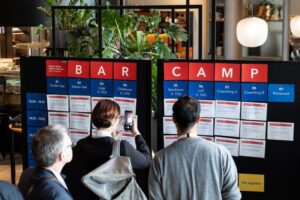 Kongressteilnehmer informieren sich an einer Infotafel über mögliche Barcamp-Themensessions.