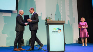 DST-Präsident Jung gratuliert per Handschlag OB Lewe und überreicht dabei eine Auszeichnung.