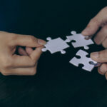Drei Hände halten jeweils ein Puzzleteil, die zusammengefügt werden sollen.