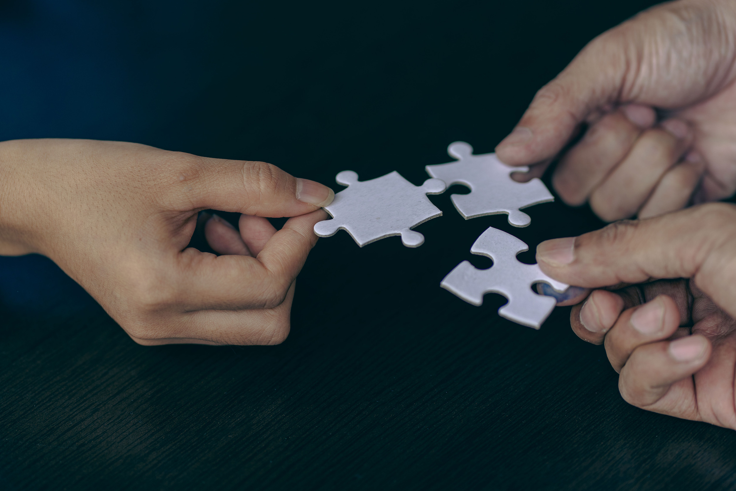 Drei Hände halten jeweils ein Puzzleteil, die zusammengefügt werden sollen.