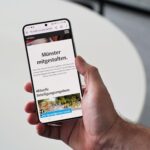 Hand hält Smartphone auf dem das Beteiligungsportal der Stadt Münster zu sehen ist