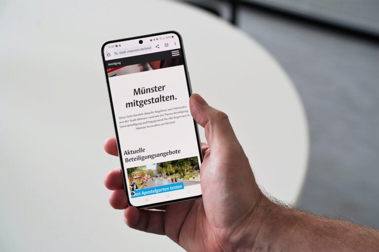 Hand hält Smartphone auf dem das Beteiligungsportal der Stadt Münster zu sehen ist