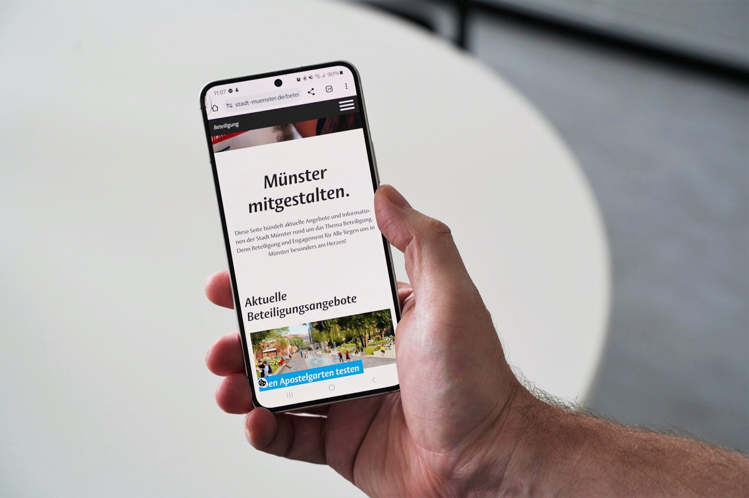 Hand hält Smartphone auf dem das Beteiligungsportal der Stadt Münster zu sehen ist