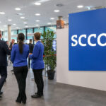 Schriftzug SCCON im Eingangsbereich einer Messehalle, daneben steht eine Personengruppe