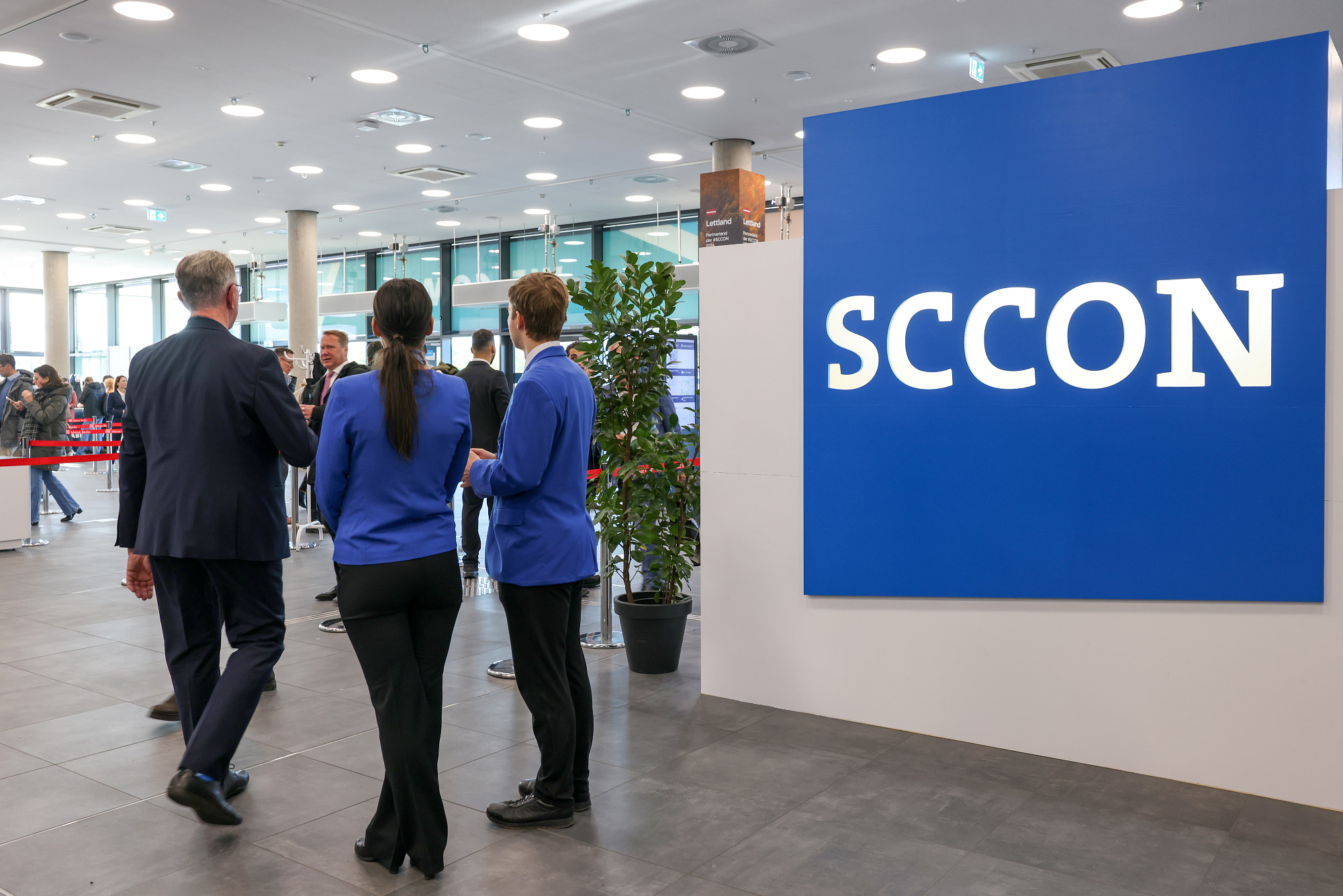 Schriftzug SCCON im Eingangsbereich einer Messehalle, daneben steht eine Personengruppe