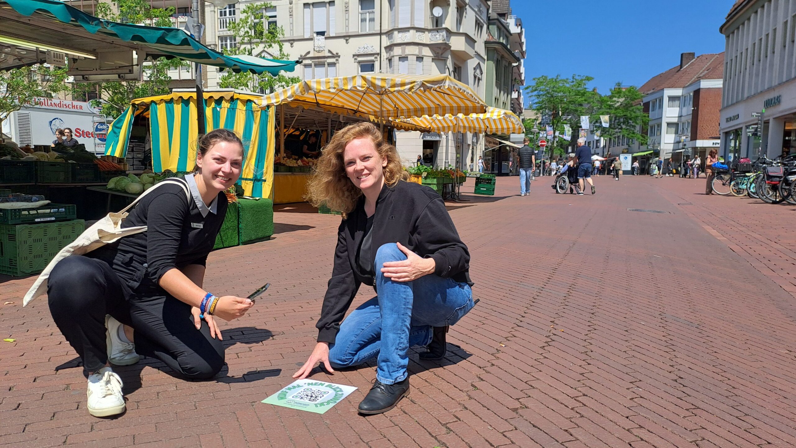 Julia Kuklik, Leiterin des Stadtarchivs Gütersloh, und Lena Jeckel, Leiterin des Fachbereichs Kultur, vor einem der QR-Codes auf dem Berliner Platz (Foto: Stadtarchiv).