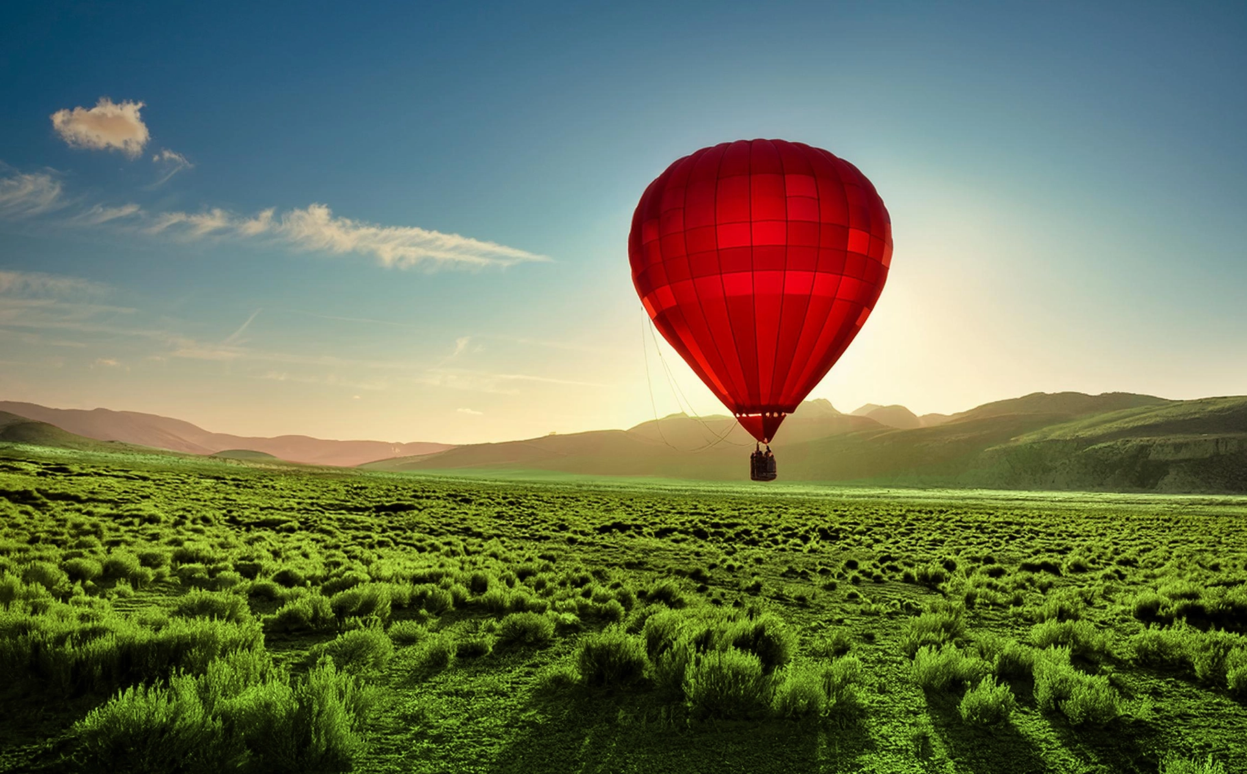 Roter Heißluftballon schwebt über grünen Feldern