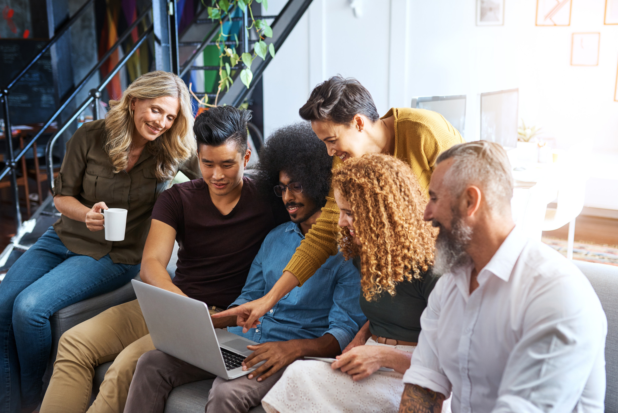 Mehrere Personen sitzen auf nebeneinander auf einem Sofa und schauen gemeinsam auf einen aufgeklappten Laptop auf dem Schoß einer der Personen.