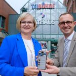 Oberbürgermeisterin Katrin Schmieder und Digitalminister Dirk Schrödter stehen nebeneinander vor dem Norderstedter Rathaus und halten gemeinsam ein Smartphone in die Kamera, auf dessen Bildschirm die neue Stadt-App zu sehen ist.