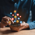 Ein Mann bedient ein Smartphone, über dem unterschiedliche Emojis schweben.