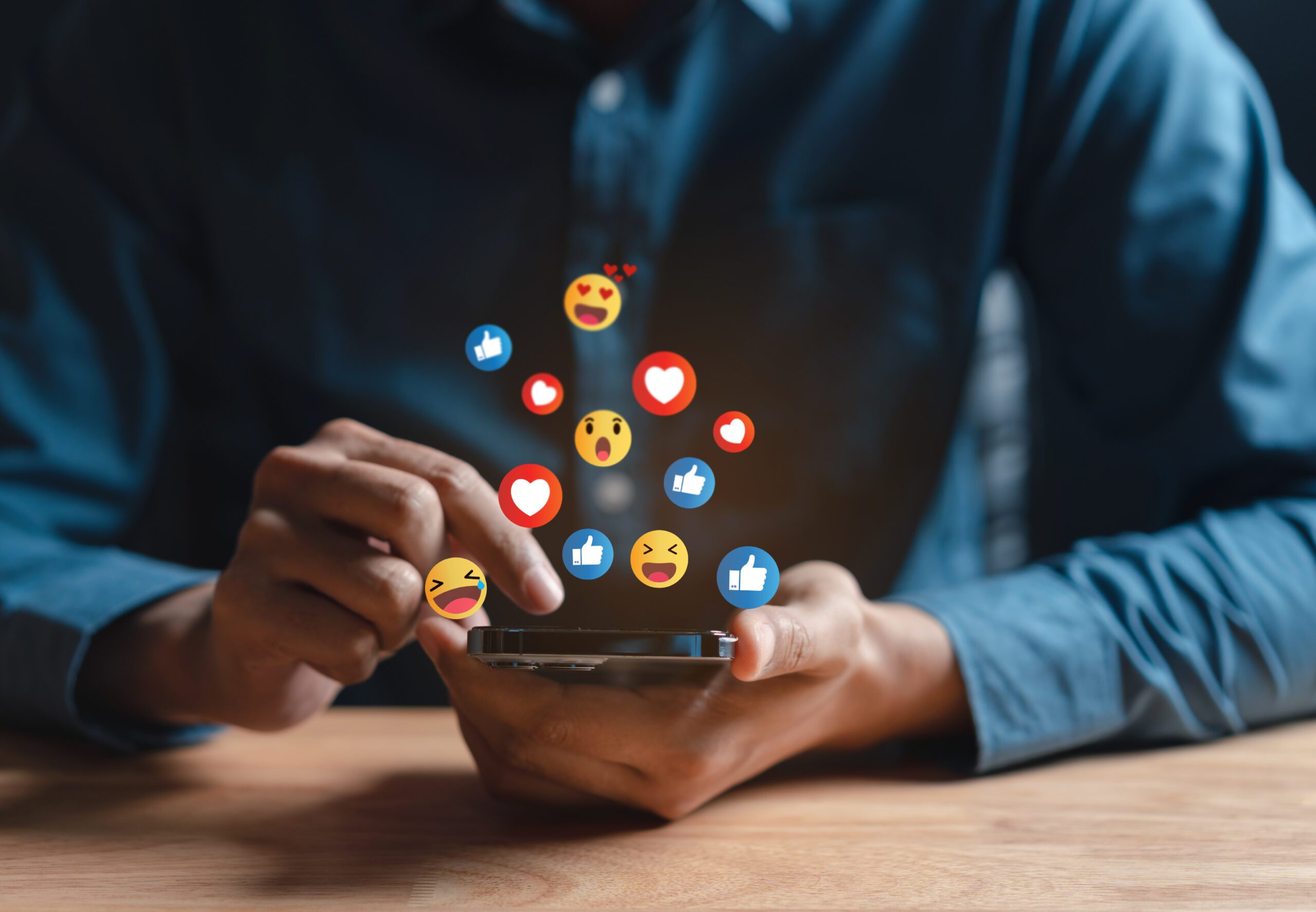 Ein Mann bedient ein Smartphone, über dem unterschiedliche Emojis schweben.