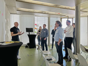 Mehrere Personen stehen in einem Raum einer anderen Person gegenüber, die etwas erklärt.