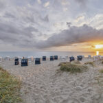 Blick auf einen Strand in der Dämmerung mit Strandkörben, davor das Meer.