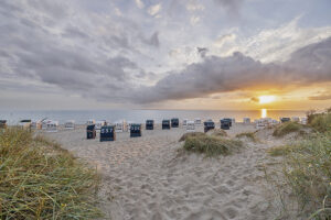 Blick auf einen Strand in der Dämmerung mit Strandkörben, davor das Meer.