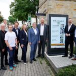 Mehrere Personen stehen nebeneinander um eine Leuchtstele im Freien versammelt.