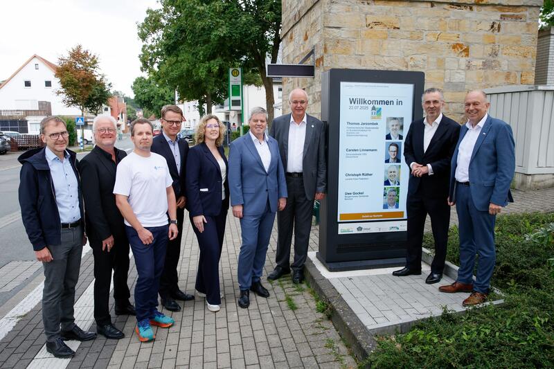Mehrere Personen stehen nebeneinander um eine Leuchtstele im Freien versammelt.