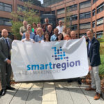 Menschen vor einem Gebäudekomplex halten das neue Logo der Smart Region Warendorf auf einem Tuchhoch