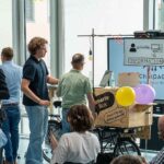 Mehrere Menschen widmen sich in einem Raum unterschiedlichen Informationstafeln und anderen Exponaten rund um die Smart City Mönchengladbach.
