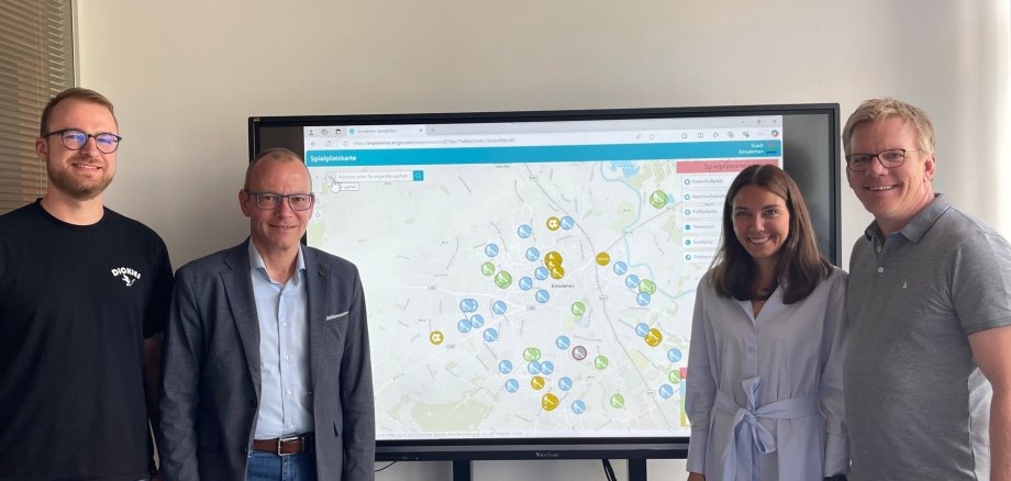 Vier Personen stehen vor einem Whiteboard, auf dem die digitale Spielplatzkarte der Stadt Emsdetten eingeblendet ist.