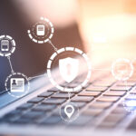 Verschwommen im Hintergrund die Nahaufnahme eines Laptops, über dessen Tastatur eine leuchtende digitale Vorhängeschloss-Schnittstelle schwebt.