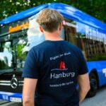Ein Mann steht vor einem Bus. Er trägt ein Shirt mit der Aufschrift Hamburg Digital für dich, die auch auf dem Bus zu sehen ist.