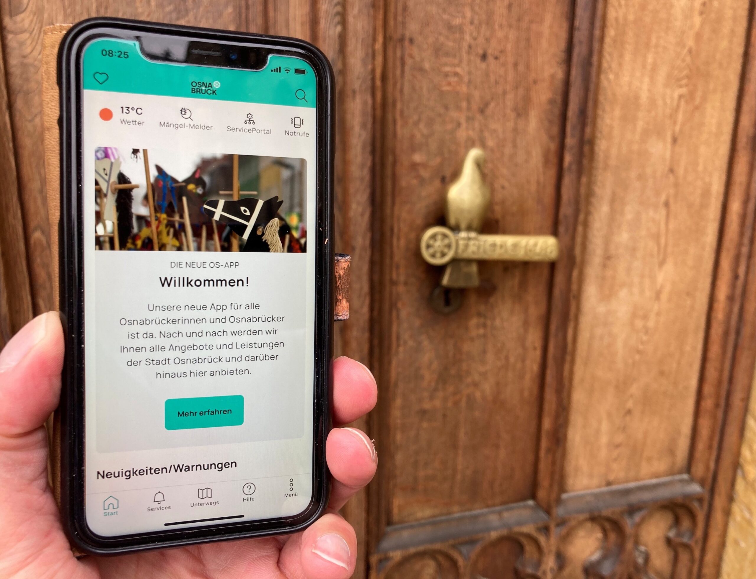 Eine Hand hält ein Smartphone auf dessen Bildschirm die Startseite der Osnabrück-App zu sehen ist.