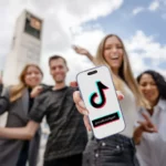 Junge Menschen stehen vor dem Stuttgarter Rathaus. In der Hand halten sie ein Smartphone mit dem TikTok Logo und dem Account-Namen @stadt.stuttgart darauf.