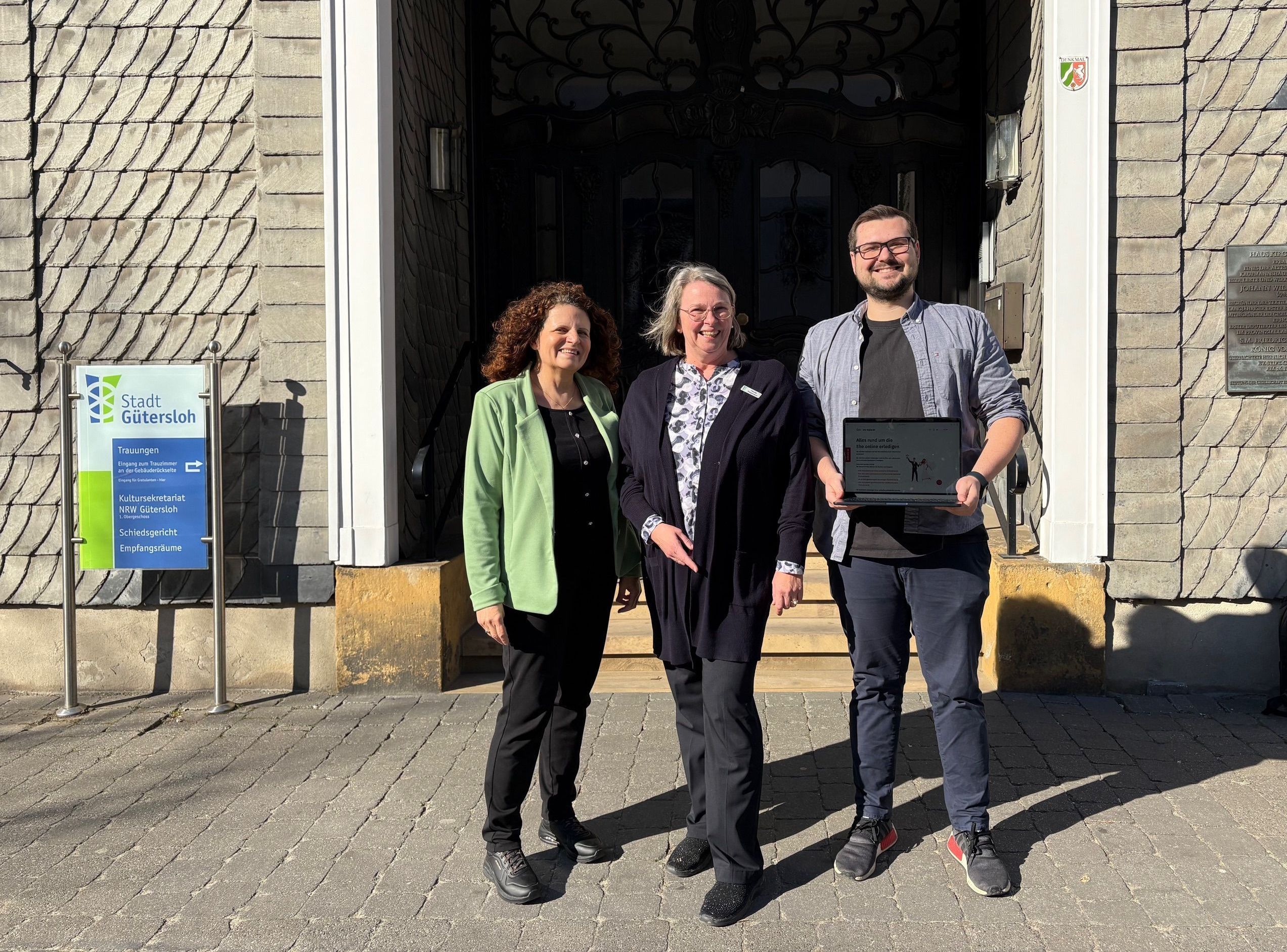 Drei Personen vor dem Gütersloher Rathaus