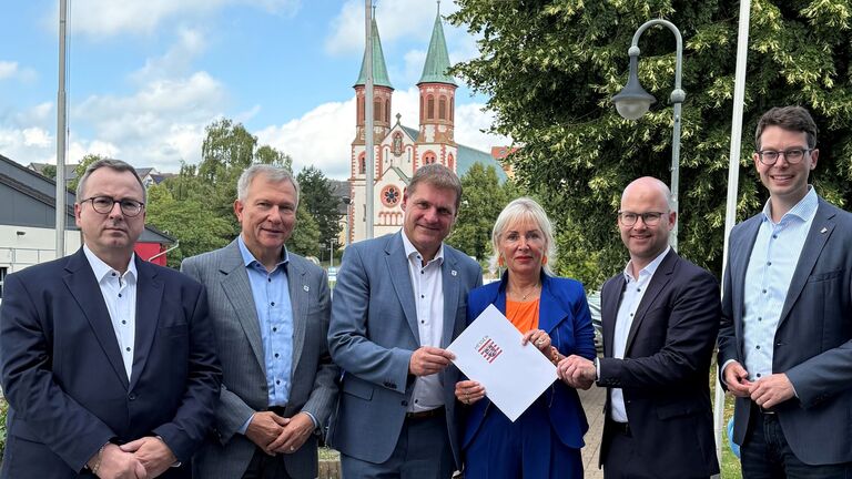 Mehrere Personen stehen nebeneinander, während Ministerin Sinemus ein Dokument überreicht.