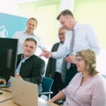 Fünf Personen sind schauen um einen PC versammelt auf dessen Bildschirm.