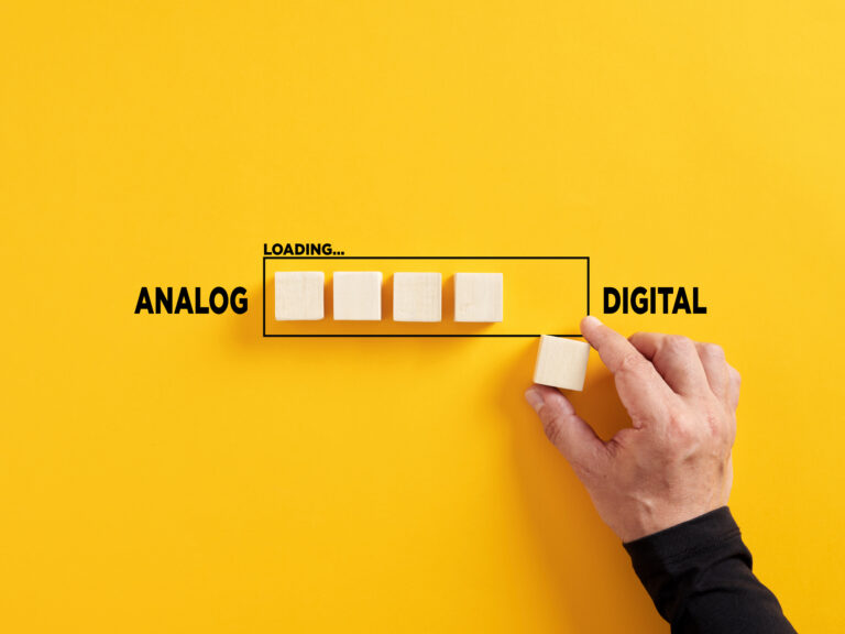 Eine Hand setzt einen Baustein in ein Diagramm ein, das den Fortschritt von Analog zu Digital angibt.