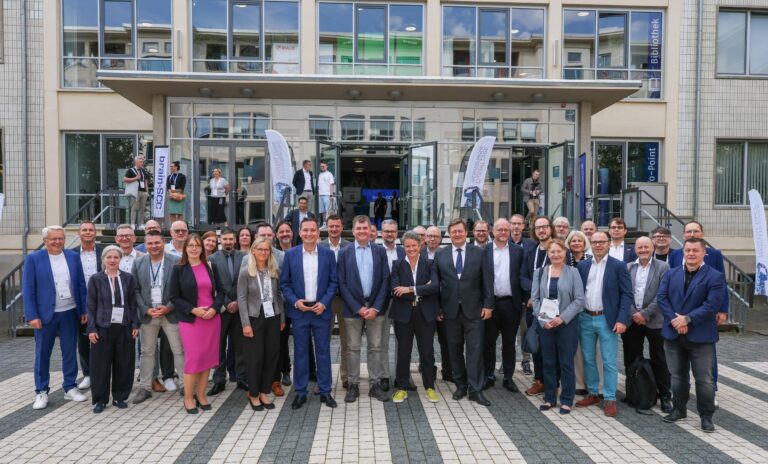 Eine große Personengruppe hat sich zum Gruppenfoto vor einem Gebäude aufgestellt.