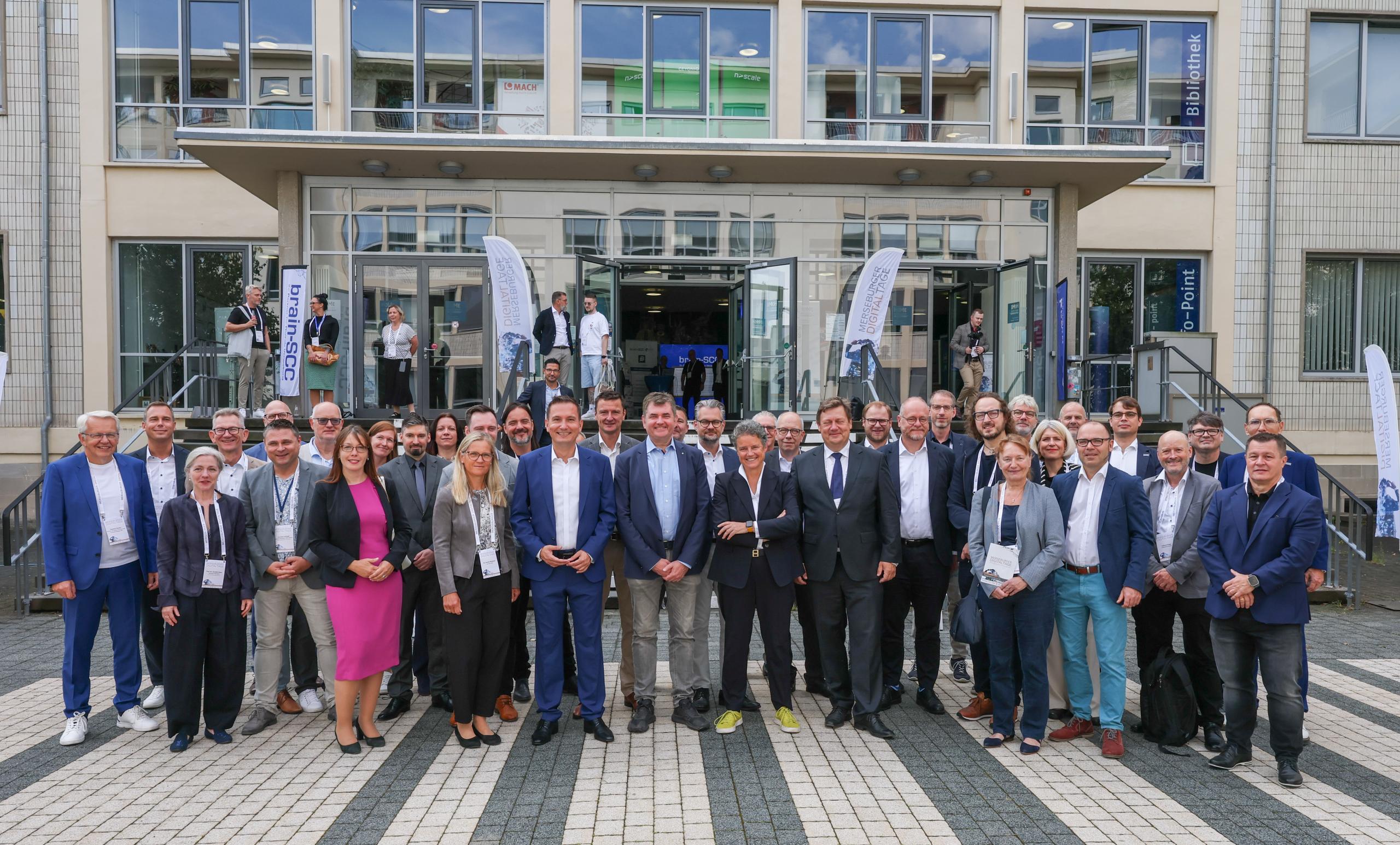 Eine große Personengruppe hat sich zum Gruppenfoto vor einem Gebäude aufgestellt.