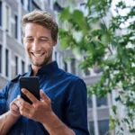 Ein Mann hantiert lächelnd an seinem Smartphone.